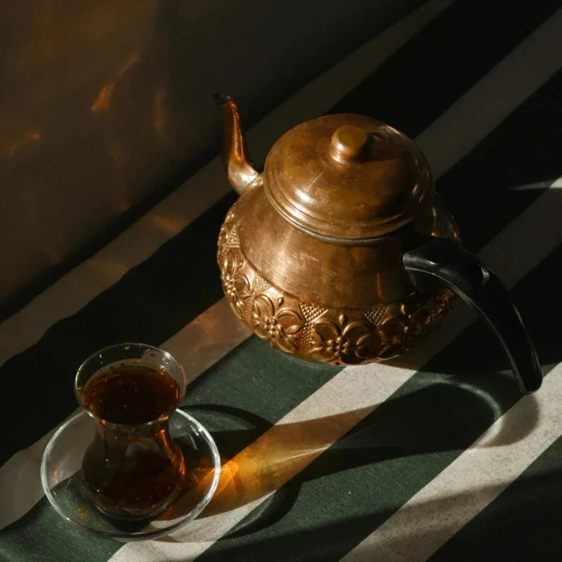 Théière en cuivre posée sur une nappe à rayures