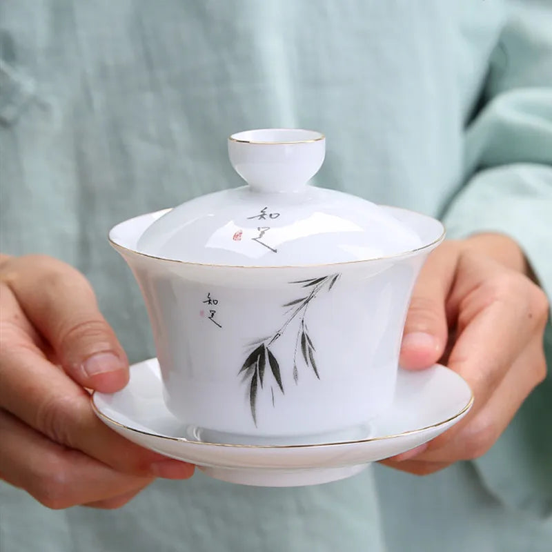Gaiwan en Porcelaine à Motifs Peint tenu entre deux main par la soucoupe 