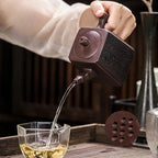 Théière Yixing Carrée versant du thé dans une tasse en verre